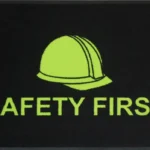 Musta värvi nailonist ohutusmatt erkkollase "Safety First" märgisega, mis on loodud tööstusruumidesse ja ladudesse, et rõhutada tööohutust ja vältida libastumisi