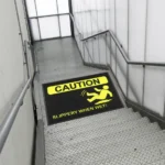 Kollase hoiatussümboliga must nailonist ohutusmatt on paigaldatud trepikoja astmele, et ennetada libastumisohtu ja juhtida tähelepanu trepile