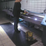 Tööline puhastamas survepesuga musta reljeefset Floorstudio kummimatti tööstuslikus köögis