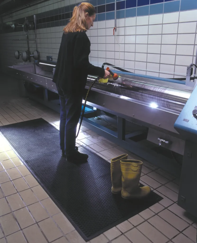 Tööline puhastamas survepesuga musta reljeefset Floorstudio kummimatti tööstuslikus köögis