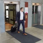 Tumehall siseruumi porimatt hotelli liftide ees, kohvriga mees peal