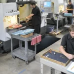 Töötajad seismas Floorstudio ergonoomilistel mattidel tööstusliku seadme juures