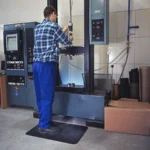 Ergonoomilised matid 41 Töömees sinises tunkedes seismas mustal ergonoomilisel matil metallitööpingi taga