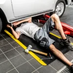 Ergonoomilised matid 51 Mehaanik parandamas autot, lamades kollaste ohutusservadega FloorStudio ergonoomilisel matil