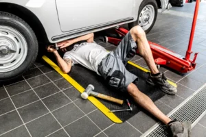 Mehaanik parandamas autot, lamades kollaste ohutusservadega FloorStudio ergonoomilisel matil