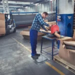 Ergonoomilised matid 52 Tööline seismas mustal FloorStudio ergonoomilisel matil tööd tegemas
