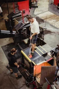 Tööline seismas platvormil kollaste servadega FloorStudio ergonoomilisel matil rasketööstuses, sädemed lendamas