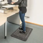 Naine seismas hallil ergonoomilisel matil reguleeritava seisulaua taga kontoris