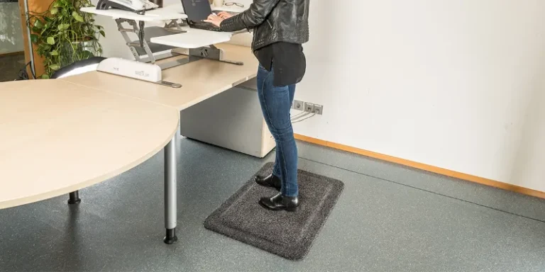 Naine seismas hallil ergonoomilisel matil reguleeritava seisulaua taga kontoris