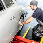 Ergonoomilised matid 66 Mehaanik põlvitamas autoteeninduses kollaste servadega FloorStudio ergonoomilisel matil auto parandamise ajal
