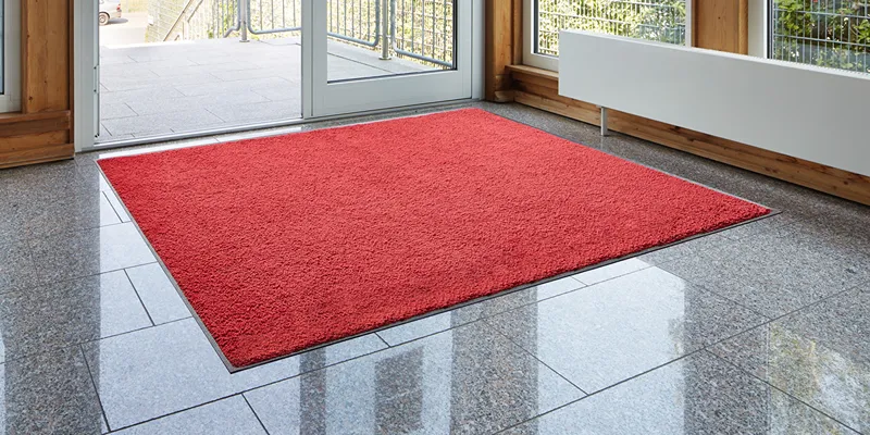Punane sissepääsu porimatt Floorstudiolt hallil plaaditud põrandal klaasukse ees.